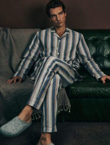 Man wearing a striped pajama set sitting on a couch.